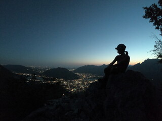 Perched high above the sprawling cityscape at twilight, a contemplative figure enjoys a moment of serene solitude, enveloped by the peaceful night and twinkling lights