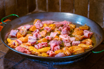 Raw chicken and pork pieces fried in a paella pan with olive oil before adding rice to cook the authentic Valencian paella.