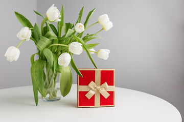Celebrating special moments with a gift and fresh white tulips indoors. Copy space