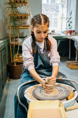 A teenage girl with long dark hair sculpts from clay on the potter's wheel .