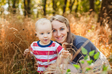 Young mother and her one-year-old baby taking pictures in autumn park bushes