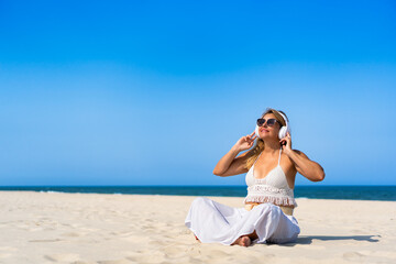 Holidays on beach with music. Beautiful middle aged woman listening to music in headphones sitting...