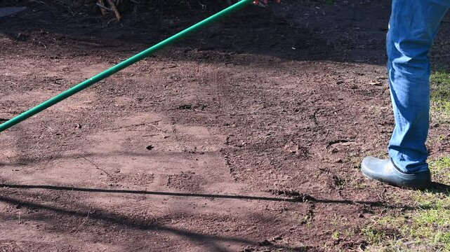 Mann ebnet mit einem Rasenrakel den Boden im Garten, um Unebenheiten auszugleichen und den Boden f&uuml;r einen perfekten Rasen vorzubereiten.