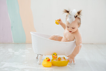 a baby bathes in a tub with foam and rubber ducklings, the concept of child hygiene, a small child...