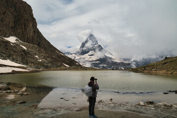 Girl hiker shooting with a selfie stick on the Matterhorn or Cervino at Lake Stellisee, Zermatt, Swiss Alps. Photograph taken in the spring season.
