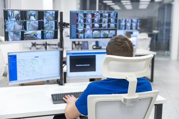 Security officer monitoring multiple surveillance screens in a high-tech control room for safety...