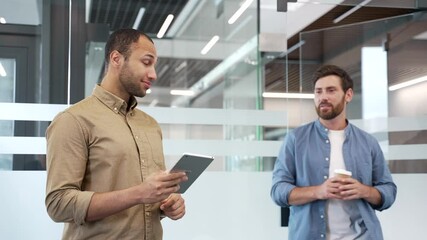 Two coworkers greet each other with a handshake in a modern business office. Happy smiling business colleagues have friendly conversation during break. Workers enjoying casual discussion with coffee