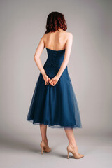 Naklejka premium Beautiful redhead woman dancing in studio on high heels, sensual portrait. Deep blue chiffon backless midi dress. Corset sleeveless classic evening gown, festive outfit. Touching look for an event