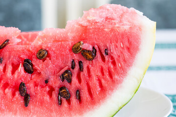 A piece of ripe juicy bright red watermelon with black seeds on a white plate. Close-up macro shot