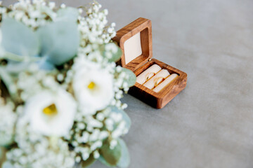 Close up of an open wooden weeding ring box with golden rings and a bride bouquet