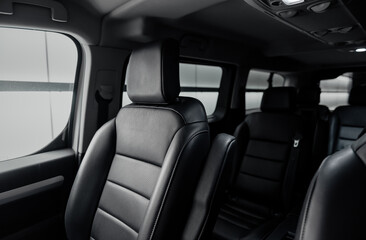 Passenger van interior with rows of leather seats at night. Front seat of mini van in focus and two rear rows in the background. 