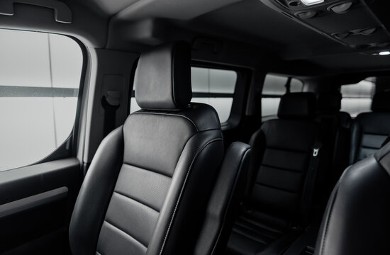Passenger van interior with rows of leather seats at night. Front seat of mini van in focus and two rear rows in the background. 