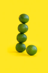 Several lime fruits stand on top of each other forming a tower on a yellow.
