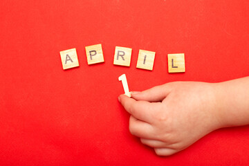 Child hand making inscription 1 April made by wooden cubes on red background
