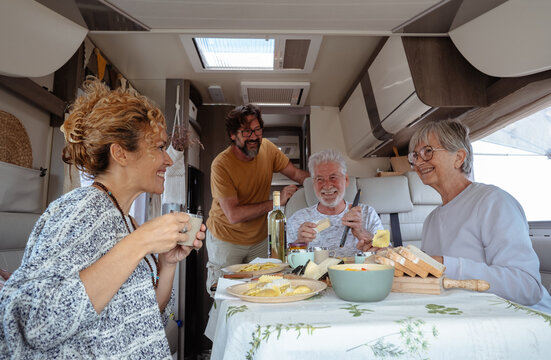 Happy family group having lunch together inside a camper van motor home. Caucasian smiling carefree modern people friends enjoying travel, free lifestyle, alternative vacation