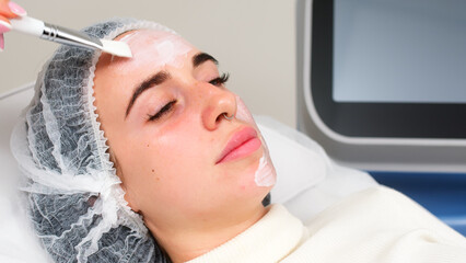 Professional beautician doing moisturizing mask on face in beauty salon on light background. Spa...
