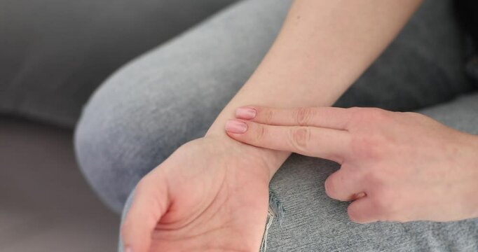 Woman hand touches own wrist with fingers checking pulse in home setting. Female monitors heart rate and overall health condition for wellbeing