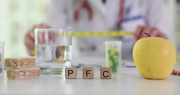 Woman doctor holds measuring tape in hands and assesses PFC of patient. Miniature wooden cubes with black letters form abbreviation PFC by apple
