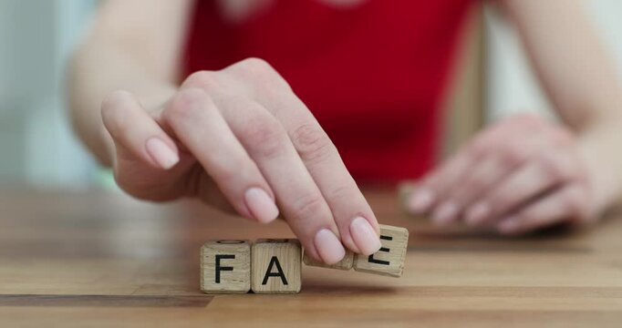 Wooden cubes arranged on smooth surface of table form word FACT. Woman changes arrangement of letters on desk to create word FAKE. Slow motion