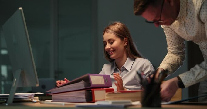 Businessman places documents into appropriate folders. Man office worker helps smiling lady secretary organize paperwork in dark office. Slow motion