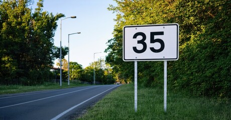 White rectangular speed limit sign bold black numbers standing quiet suburban road glowing softly streetlights