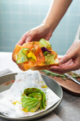 In the cafe setting, hold the cucumber, avocado, and smoked salmon sandwich with both hands