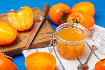 Persimmon jam with slices of ripe persimmon on wooden textured table. Delicious persimmon jam. Marmalade. Healthy sweets. Vegan. Close-up. Space for text. Copy space.