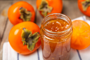 Persimmon jam with slices of ripe persimmon on wooden textured table. Delicious persimmon jam. Marmalade. Healthy sweets. Vegan. Close-up. Space for text. Copy space.
