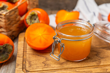 Persimmon jam with slices of ripe persimmon on wooden textured table. Delicious persimmon jam. Marmalade. Healthy sweets. Vegan. Close-up. Space for text. Copy space.
