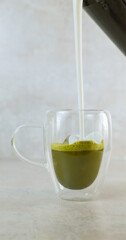 Pouring Frothed Milk into Matcha Tea in Glass Mug slow motion vertical shot