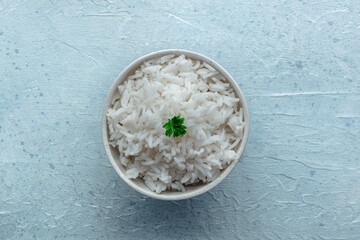 White rice, cooked. A bowl of boiled long grain rice, a simple side dish, with fresh parsley leaves, overhead flat lay shot