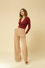 Series of studio photos of young female model wearing simple beautiful outfit, red v neck shirt and beige wide leg trousers