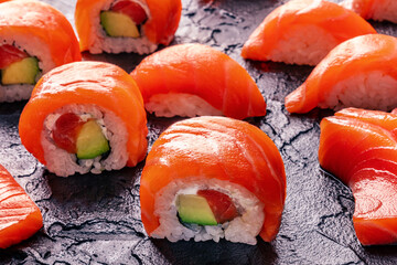 Salmon uramaki sushi roll and nigiri set on a black slate background, a close-up