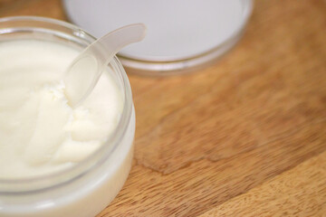 A jar of cream or coconut oil with a spoon on a wooden tray, ideal for face, body, and hair care, providing nourishment, hydration, and spa treatments.
