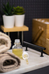 A serum bottle on a marble tray with a soft towel, set against a black background and wooden elements,  face care, hydration, nourishment, and spa treatments, promoting skin health and beauty.