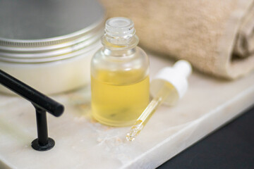 A serum bottle on a marble tray with a soft towel, set against a black background and wooden elements,  face care, hydration, nourishment, and spa treatments, promoting skin health and beauty.