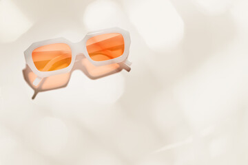 Top view trendy transparent peach orange colored sunglasses on beige background, shadow and glare...