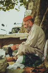 A poor old shoe man cobbler sitting under a tree in a local street shop of Pakistan with his tools while repairing an old shoe