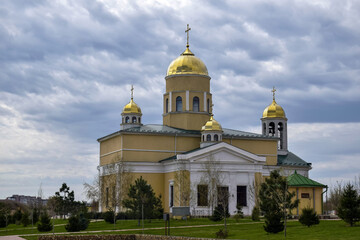 Christian temple, church with green lawn in front of it and gilded domes, crosses against cloudy sky. Religious building. Copy space for text.
