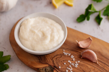 Lebanese Garlic sauce Toum or Salsat toum contains garlic, salt, olive oil and lemon juice on wooden board. Traditional Middle East food. Food photography.