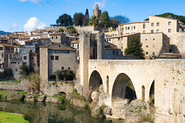 Puente medieval y centro hist&oacute;rico de Besal&uacute; con edificaciones de piedra reflejadas en el r&iacute;o Fluvi&agrave;.