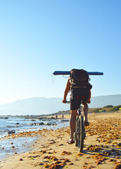 Cyclist carrying a backpack and tent pedaling along the seashore at Bolonia Beach near Tarifa, Coast of Light Cadiz, Andalusia, southern Spain.