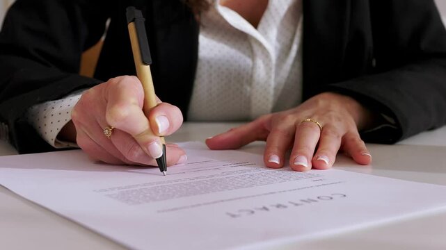 Young professional woman carefully signing critical legal contract. Close-up view of a businesswoman diligently signing a legal document at her office desk