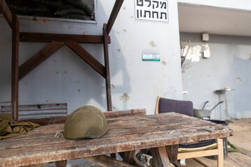A soldier's helmet lies on a wooden table at the entrance to a bomb shelter. On the wall, the word 