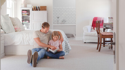 Obraz premium Father And Daughter Sitting On Floor In Cool Bedroom Reading Book Together