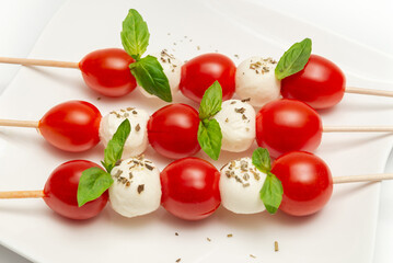 Caprese skewers snacks with tomatoes and basil leaves on a white plate