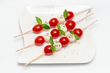 Caprese skewers with tomatoes on a plate on a white background