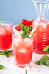 Homemade watermelon lemonade, sweet refreshing summer drink, iced watermelon juice with mint decor and striped straw, light blue and wooden background, copy space 