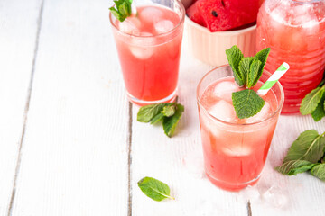 Homemade watermelon lemonade, sweet refreshing summer drink, iced watermelon juice with mint decor and striped straw, light blue and wooden background, copy space 