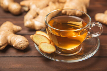 Cup of hot ginger tea with slices of ginger root on wooden background. Warming drink. Alternative...